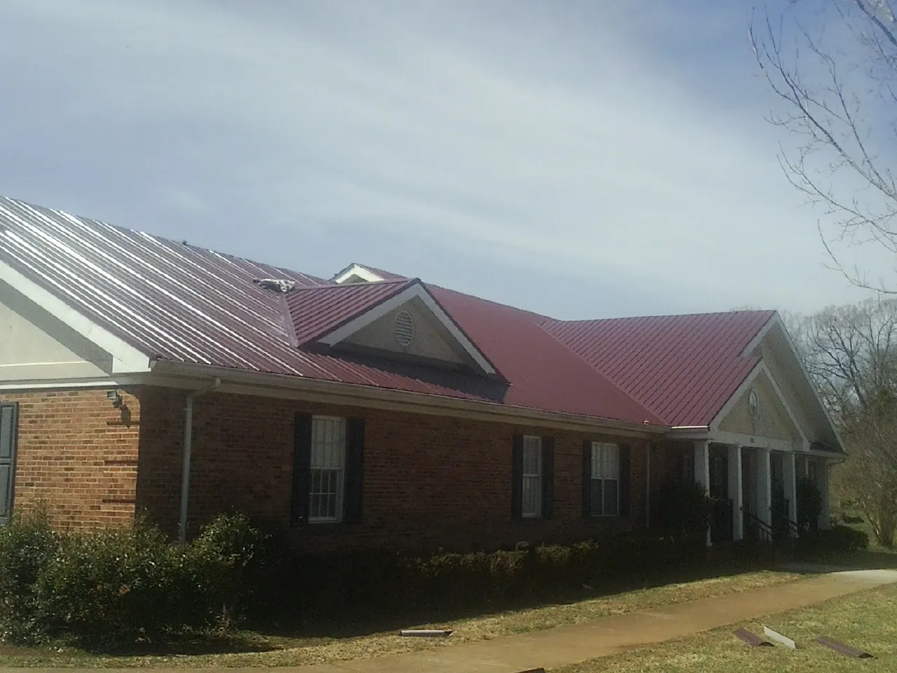 Red metal roof with gabled entries on a long brick building, from a Hail Damage Roof Repair job in Stony Point